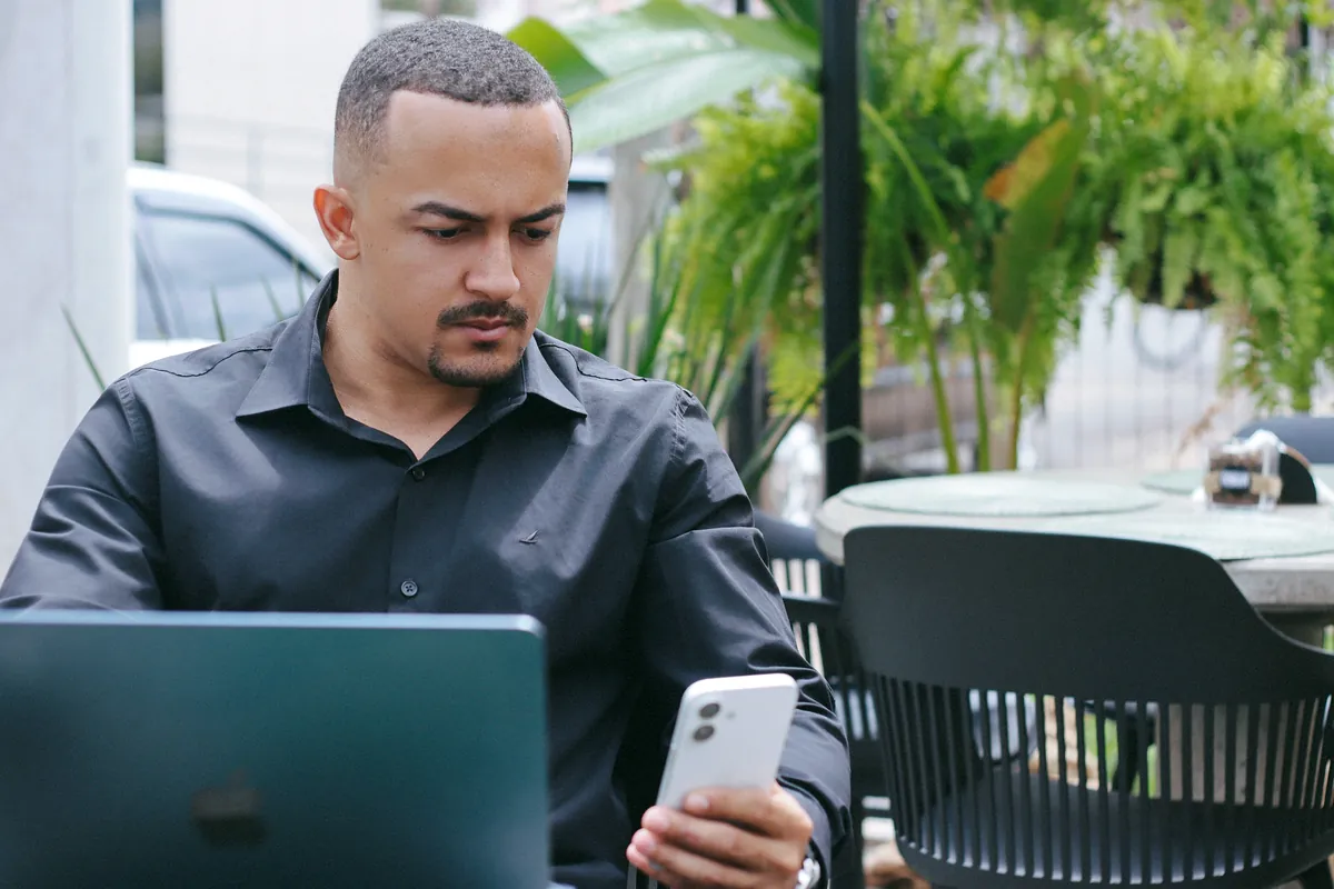 Victor Oliveira consultando o celular enquanto trabalha no notebook